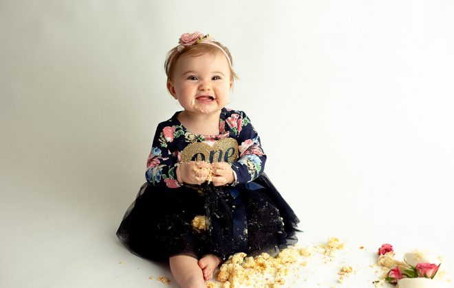 smiling toddler eats cake during one year photo session