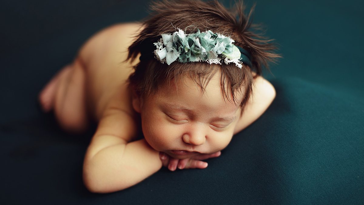 sleeping newborn posed chin on wrists on emerald green backdrop