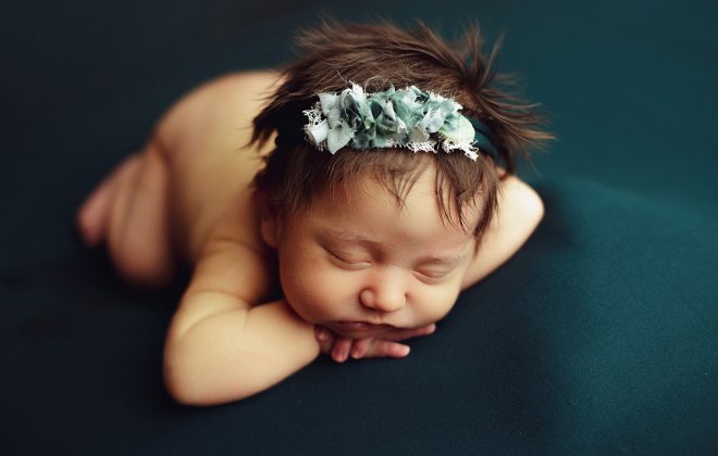 sleeping newborn posed chin on wrists on emerald green backdrop