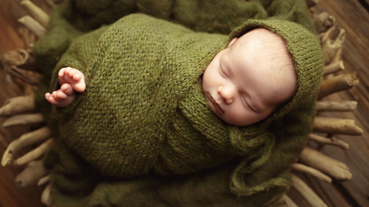 newborn boy wrapped in green posed in driftwood bowl