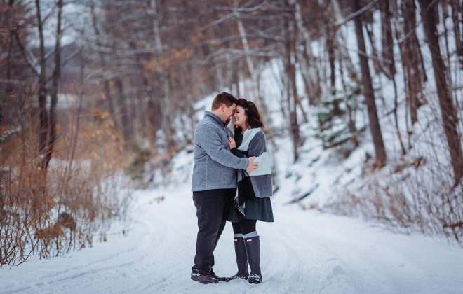 husband and wife stand together on a snowy path in marquette michigan