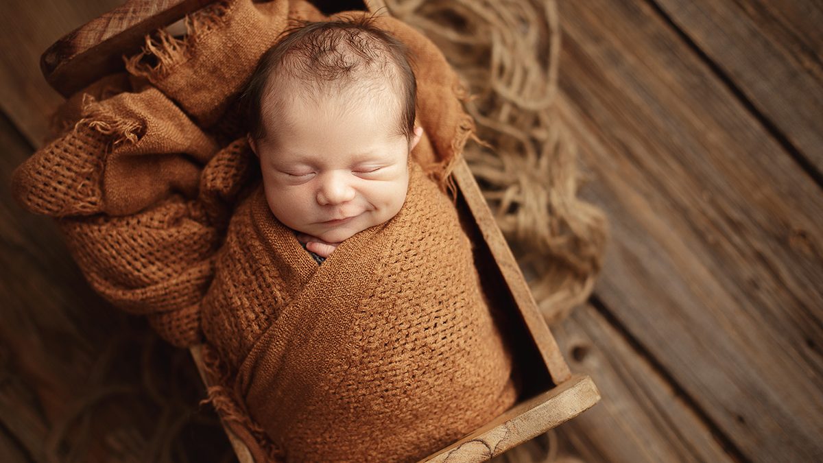 smiling newborn boy wrapped in burnt orange with rustic layers