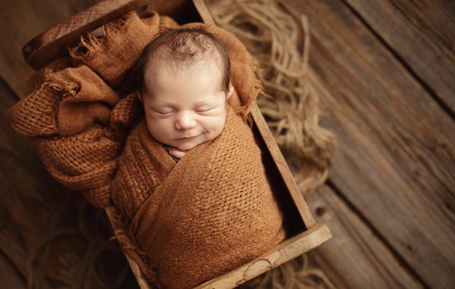 smiling newborn boy wrapped in burnt orange with rustic layers