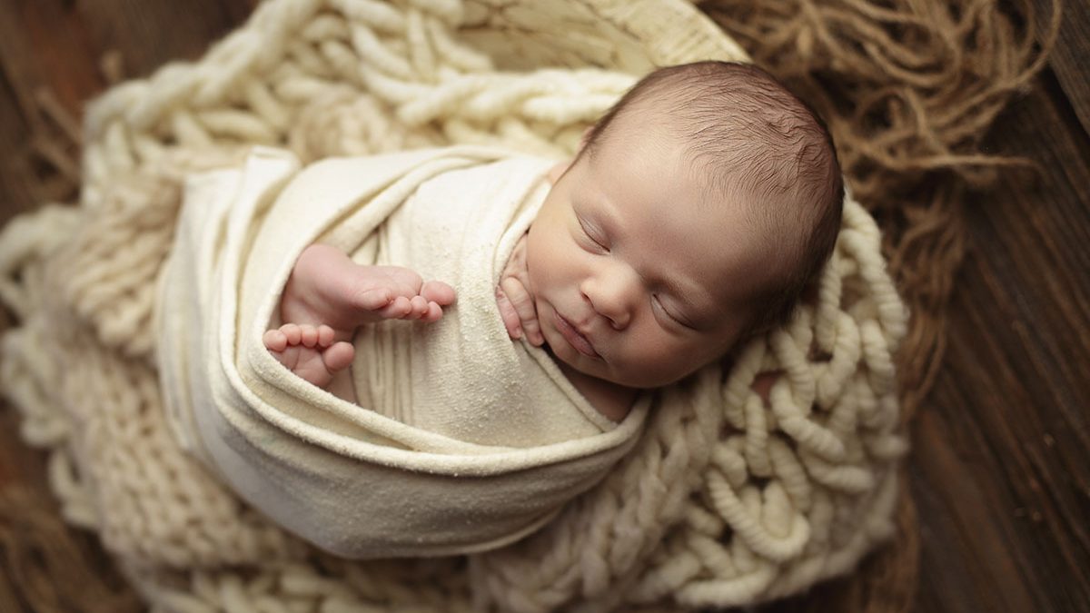 newborn boy posed in bowl with warm neutral props