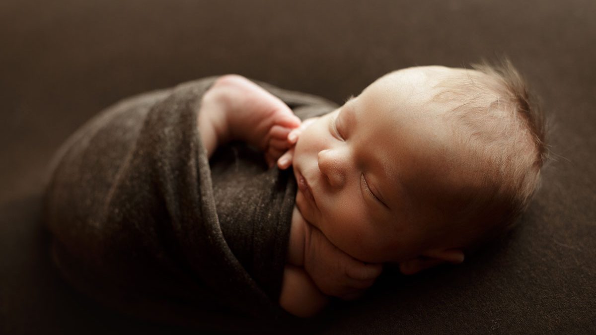 baby boy posed on dark green backdrop backlit