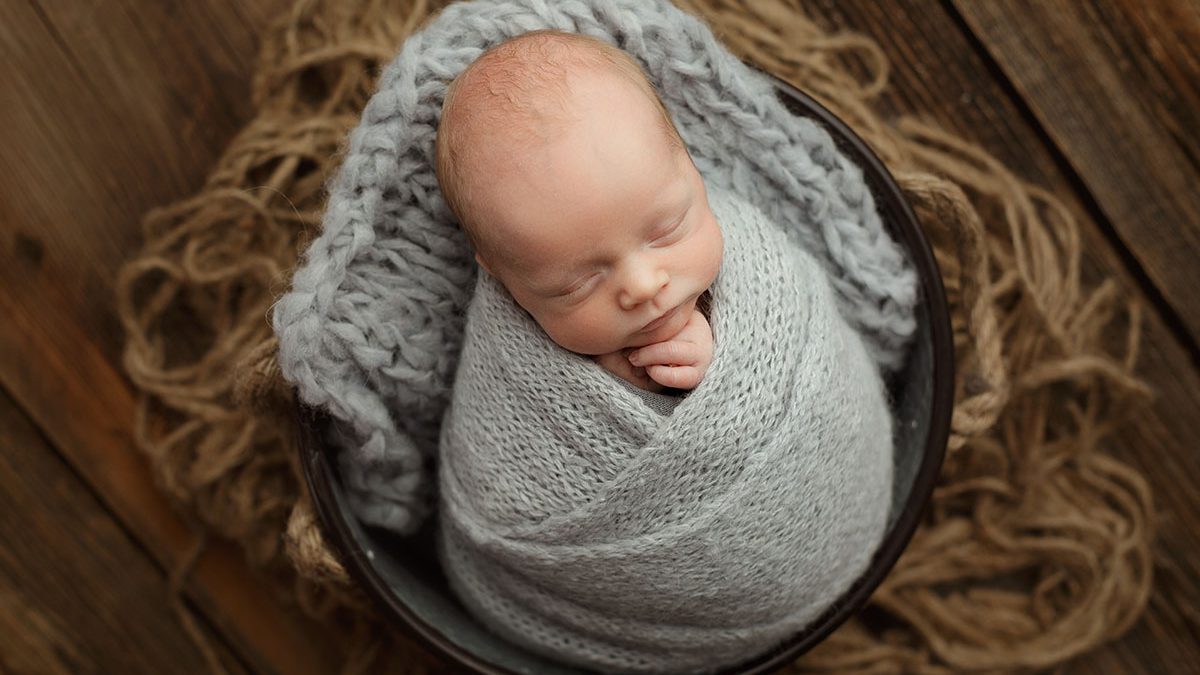 newborn boy wrapped in gray brushed alpaca knit wrap posed in galvanized bucket on rustic barn wood backdrop