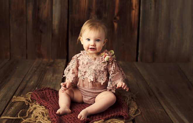 one year milestone session in escanaba michigan photo studio with toddler girl in pink ruffled outfit on rustic barn wood backdrop
