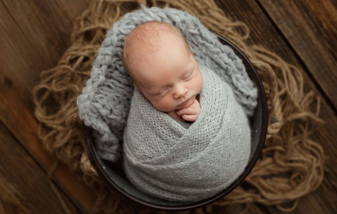 newborn boy wrapped in gray brushed alpaca knit wrap posed in galvanized bucket on rustic barn wood backdrop