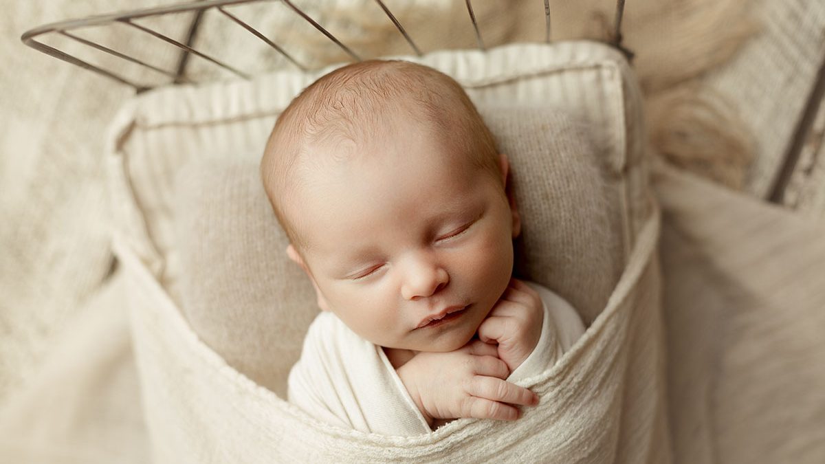 newborn boy posed on antique wire bed on cream rustic barn wood backdrop