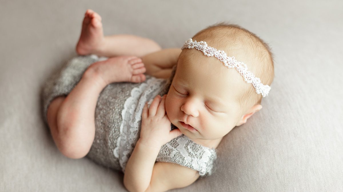 newborn girl posed on gray backdrop with gray onesie