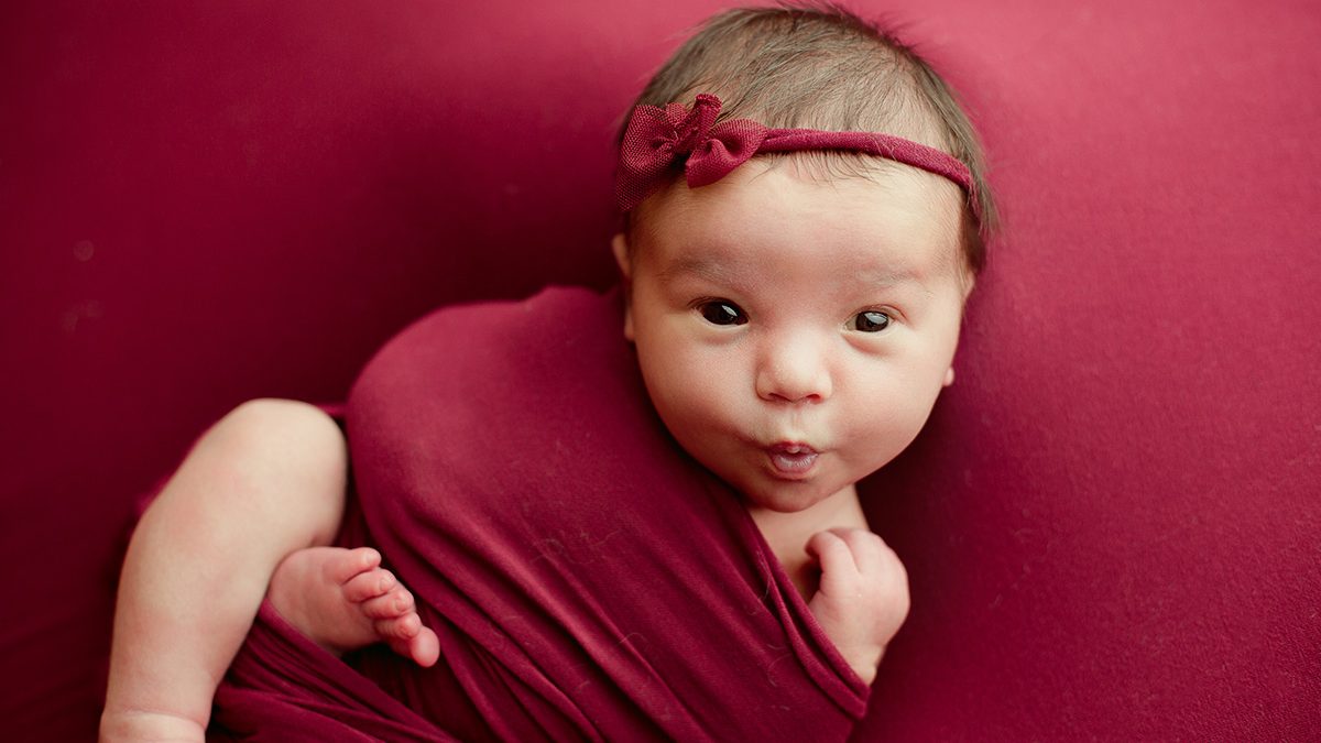 newborn girl posed on cranberry backdrop