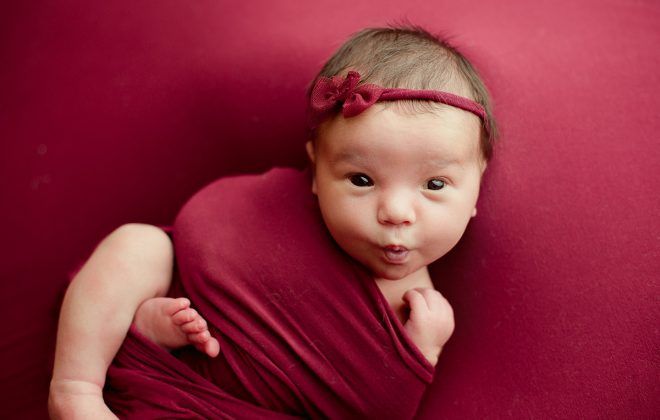 newborn girl posed on cranberry backdrop