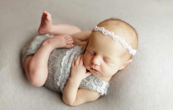 newborn girl posed on gray backdrop with gray onesie