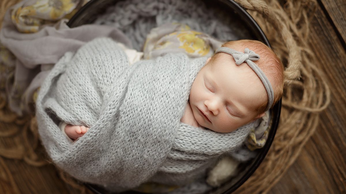 baby girl wrapped in soft knit wrap with gray and yellow floral accent fabric posed on rustic barn wood backdrop