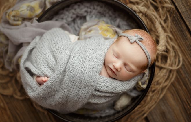 baby girl wrapped in soft knit wrap with gray and yellow floral accent fabric posed on rustic barn wood backdrop