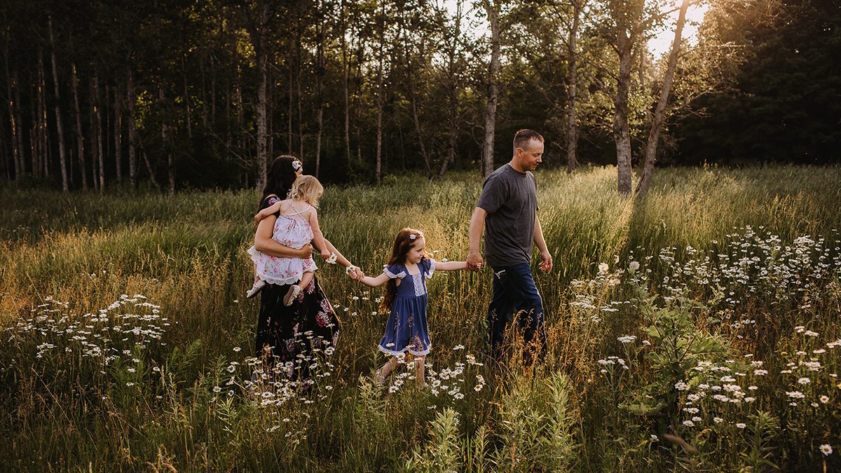 family walks through flowered field with beautiful backlit golden sunlight during outdoor family photo session in escanaba michigan