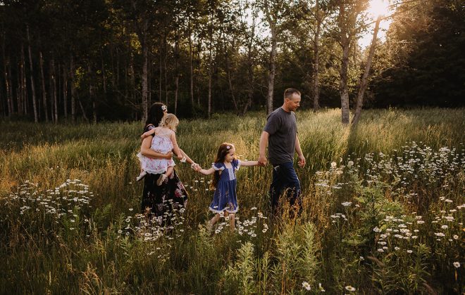 family walks through flowered field with beautiful backlit golden sunlight during outdoor family photo session in escanaba michigan