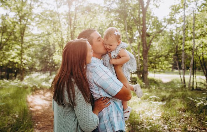 parents snuggle their happy toddler girl during family photos in michigan's upper peninsula