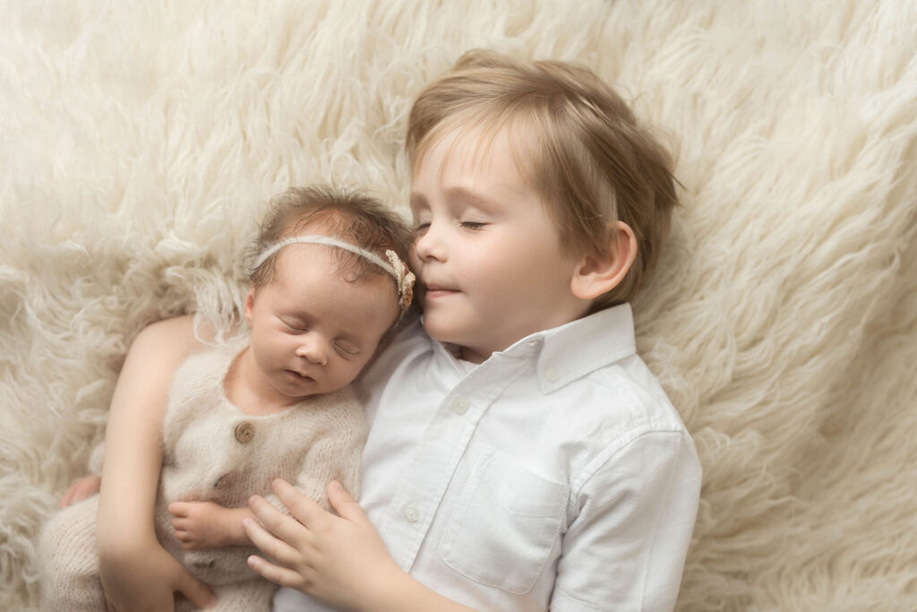 school aged brother holding his newborn sister on a cream backdrop