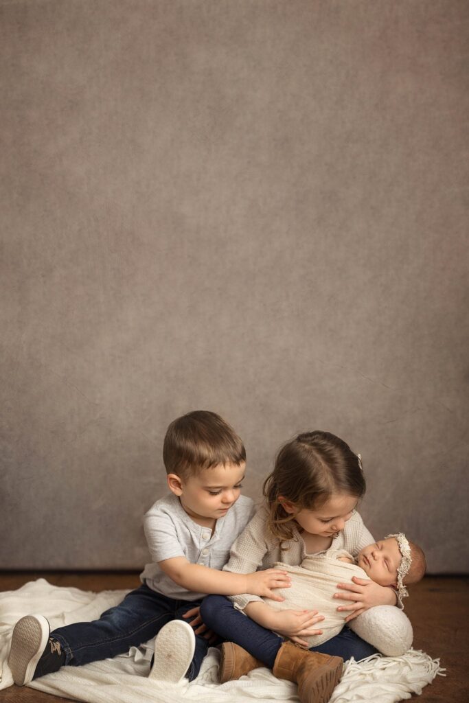 siblings holding their new baby sister during newborn photos