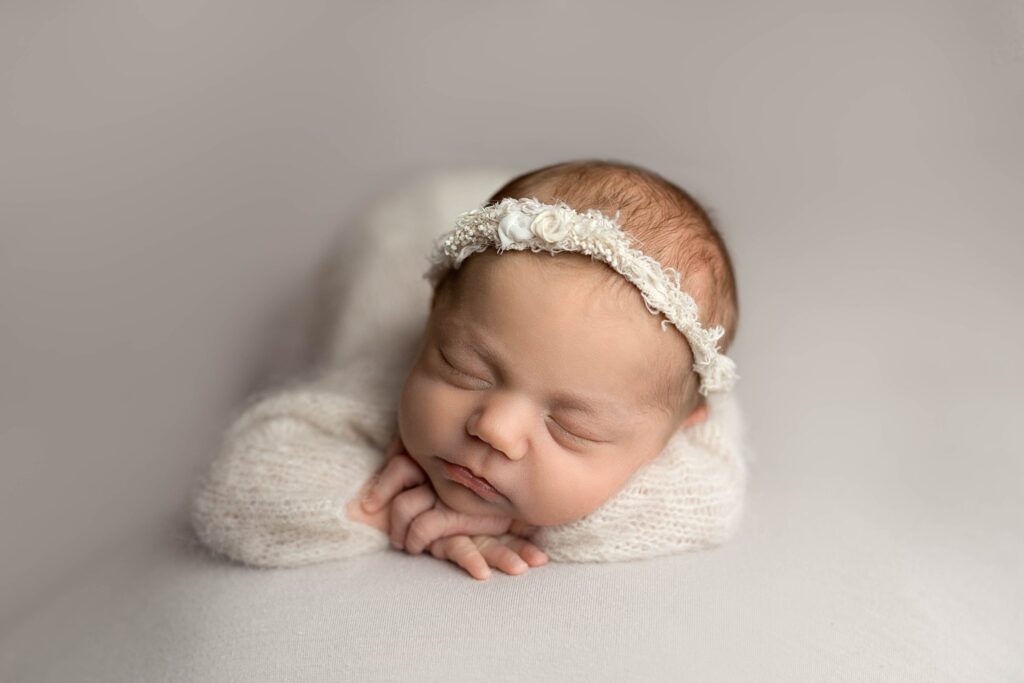 simple, clean image of a newborn posed on her tummy, on a white background wearing a white knit onesie.
