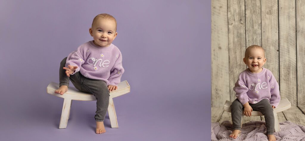 One year old posing on a white bench wearing a purple sweater, smiling at the camera.