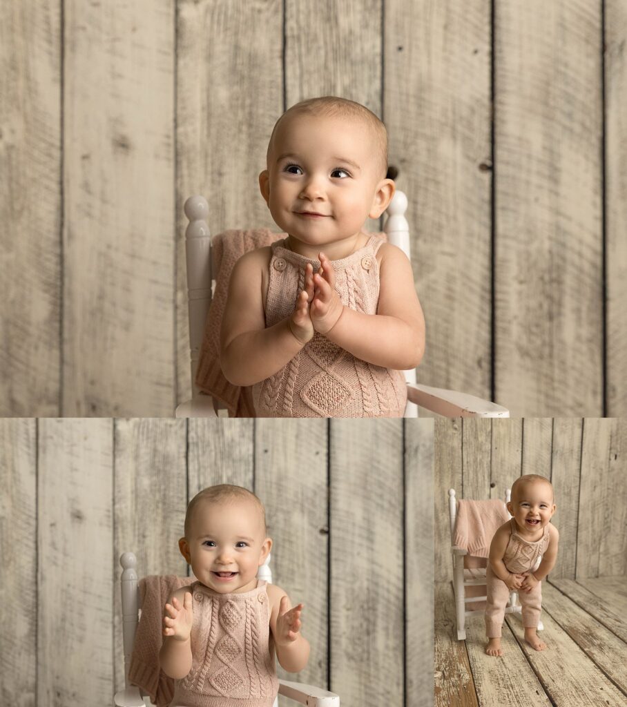 One year old in pink knit overalls, sitting in a white rocking chair and smiling.