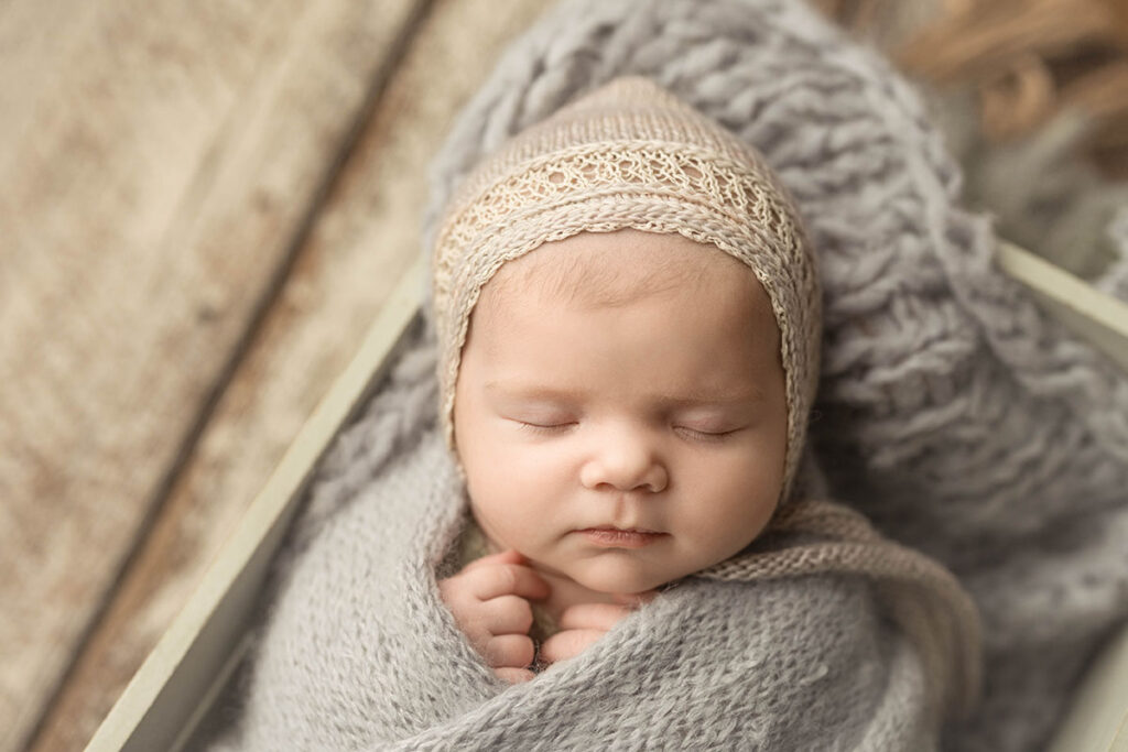 newborn baby wrapped in soft gray Angora wrap wearing a lacy bonnet.