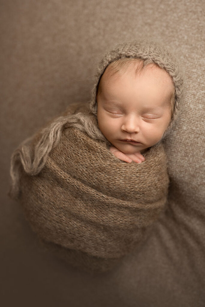 newborn baby wrapped in a soft brown alpaca knit wrap with a matching bonnet.