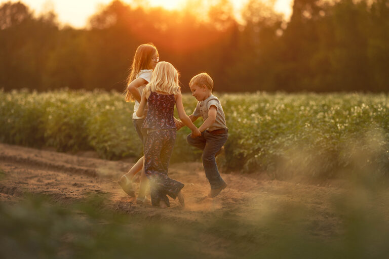 three kids play on a dirt trail through a potato field at sunset, during Escanaba Michigan extended family photoshoot.